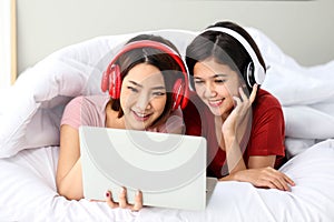 Happy Couple  asia woman wear headphones and enjoy musics playing mobile phone and tablet in bedroom