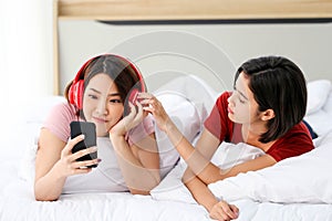 Happy Couple  asia woman wear headphones and enjoy musics playing mobile phone and tablet in bedroom photo