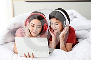 Happy Couple  asia woman wear headphones and enjoy musics playing mobile phone and tablet in bedroom