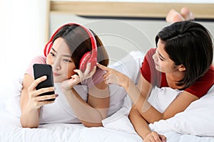 Happy Couple  asia woman wear headphones and enjoy musics playing mobile phone and tablet in bedroom photo