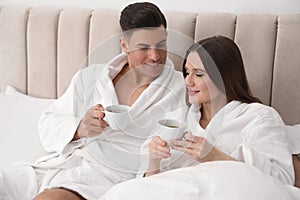 Happy couple in bathrobes with coffee on bed at home