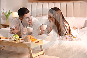 Happy couple in bathrobes having breakfast on bed