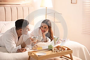 Happy couple in bathrobes having breakfast at home