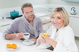 Happy couple in bathrobes having breakfast in kitchen