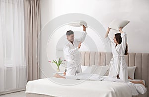 Happy couple in bathrobes having pillow fight on bed
