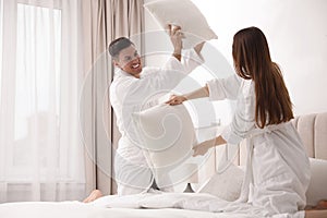 Happy couple in bathrobes having pillow fight on bed