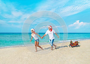 Happy couple at beach in red santa hats with gifts, sled and dec