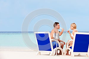 Couple On Beach Relaxing In Chairs And Drinking Champagne