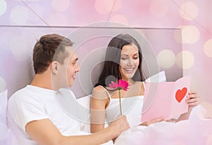 Happy couple in bed with postcard and flower