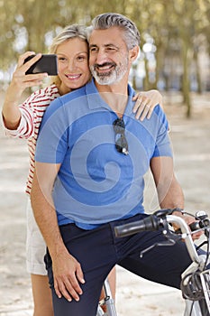 happy couple with bicycles taking selfie in summer park