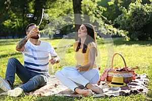 Happy couple blowing soap bubbles in park on spring day