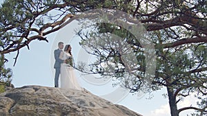 A happy couple of brides stand on the mountain with their backs to the camera and look into the distance at the