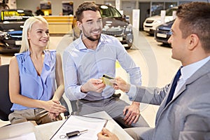 Happy couple with car dealer in auto show or salon