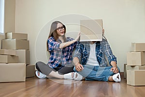 Happy couple with cardboard boxes on their heads sitting on floor after the moving house.