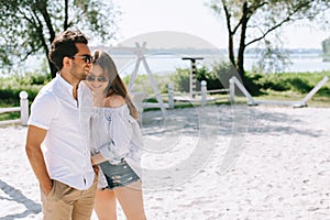 happy couple in casual clothes and sunglasses standing on sandy