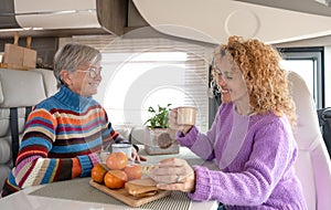 Happy couple of caucasian women multigenerational family sitting inside a camper van motor home looking enjoying coffee break.