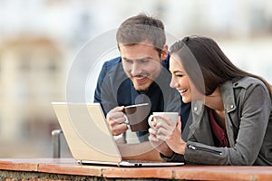 Happy couple checking laptop content on a balcony