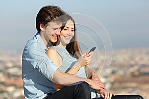 Happy couple checking phone sitting in the city outskirts photo