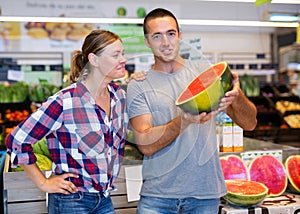Happy couple choosing ripe sweet watermelon in supermarket