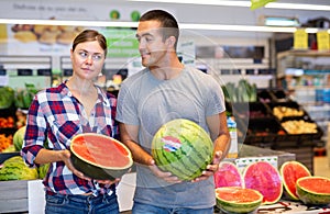 Happy couple choosing ripe sweet watermelon in supermarket