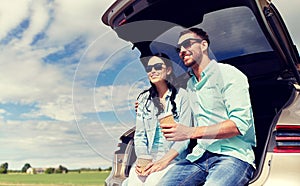 Happy couple with coffee at hatchback car trunk
