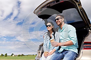 Happy couple with coffee at hatchback car trunk