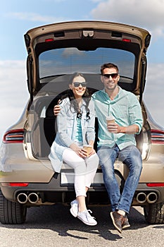 Happy couple with coffee at hatchback car trunk