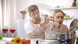 Happy couple cooking together in kitchen, female tasting soup, healthy food