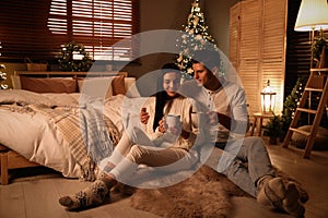 Happy couple with cups in festively decorated bedroom. Christmas celebration