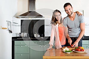 Happy Couple Cutting Vegetables At Kitchen Counter