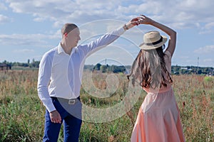 happy couple dancing in the field. brunette in cream dress and bald man in white shirt and blue pants. love story