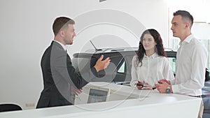 Happy couple with dealer shaking hands in car dealership.