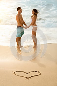 Happy couple with draw heart on sandy beach