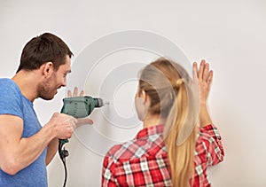 Happy couple with drill perforating wall at home