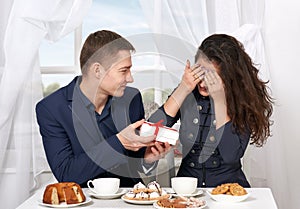 Happy couple drinking coffee and having fun, give gifts near window with a sky view - love and holiday concept