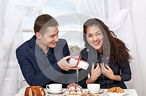 Happy couple drinking coffee and having fun, man give very funny gifts - love and holiday concept