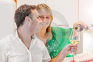 Happy couple is drinking a glass of white wine in the kitchen