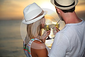 Happy couple with drinks enjoying sunset view on the sea