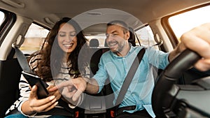 Happy couple driving car and using cell phone