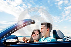 Happy couple driving convertible along seaside.