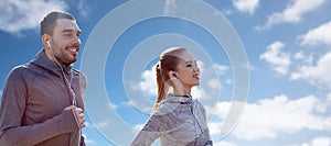 Happy couple with earphones running over blue sky