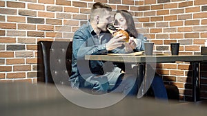 Happy couple eating burgers and having fun together in cafe