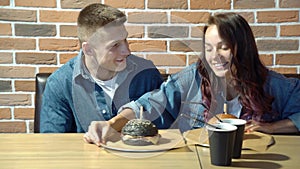 Happy couple eating burgers and having fun together in cafe