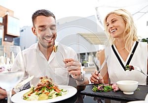 Happy couple eating dinner at restaurant terrace