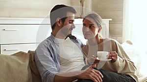 Happy couple embracing talking drinking coffee tea sitting on sofa