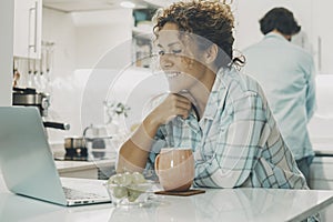Happy couple enjoy time at home together doing different work. Man cleaning kitchen and woman using laptop for work or online