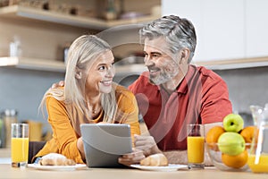 Happy couple enjoying healthy breakfast, using digital tablet