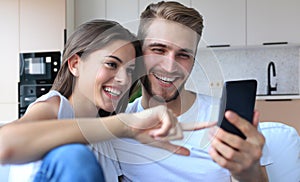 Happy couple enjoying media content in a smart phone sitting on a couch at home.