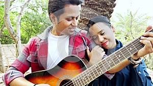 Happy couple enjoying music together outdoors with a man playing guitar and a woman leaning on his shoulder