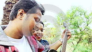 Happy couple enjoying music together outdoors with a man playing guitar and a woman leaning on his shoulder